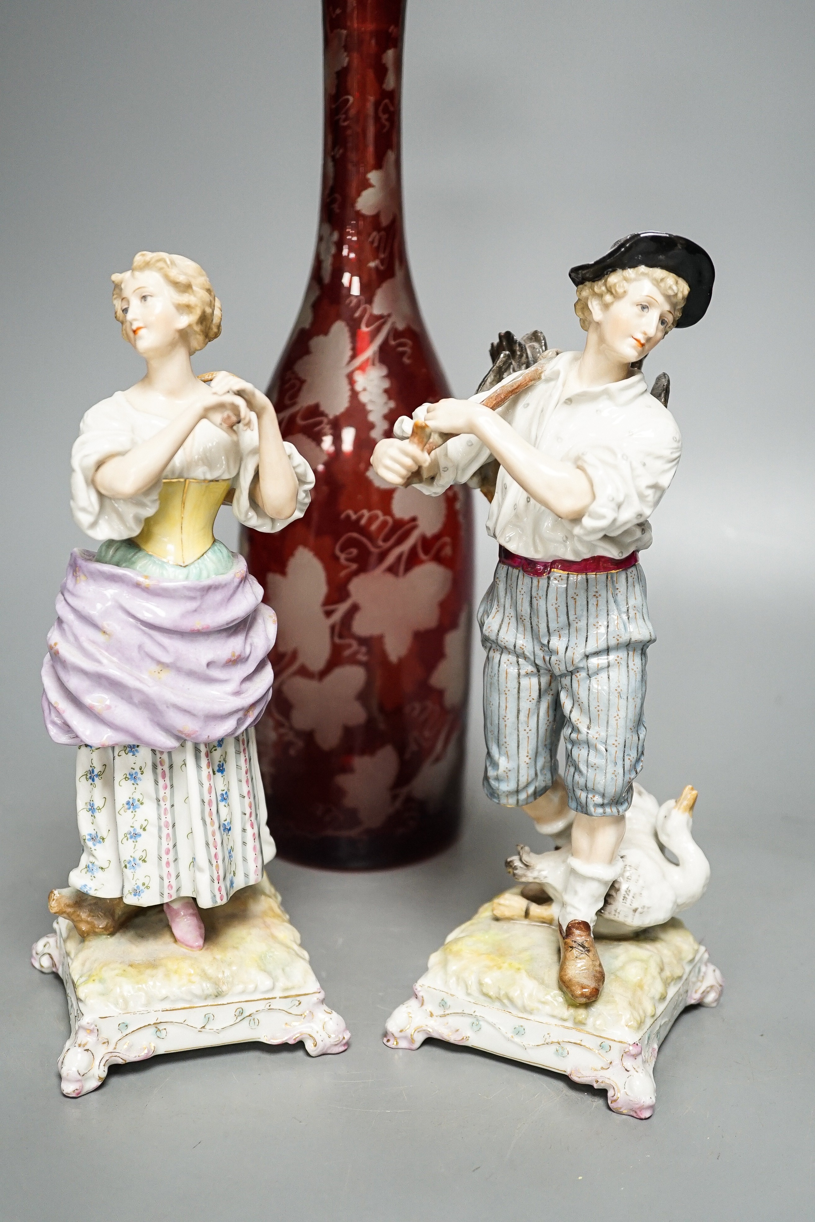 A late 19th century Bohemian wheel engraved ruby glass decanter and a pair of continental porcelain figures, decanter 37 cms high, including stopper.